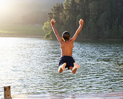 Barn hoppar från brygga ner i en sjö