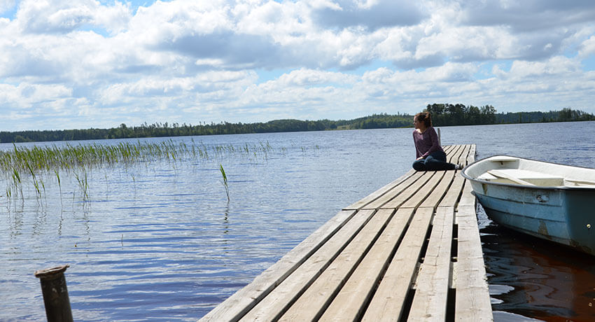 En person sitter på en brygga vid en sjö